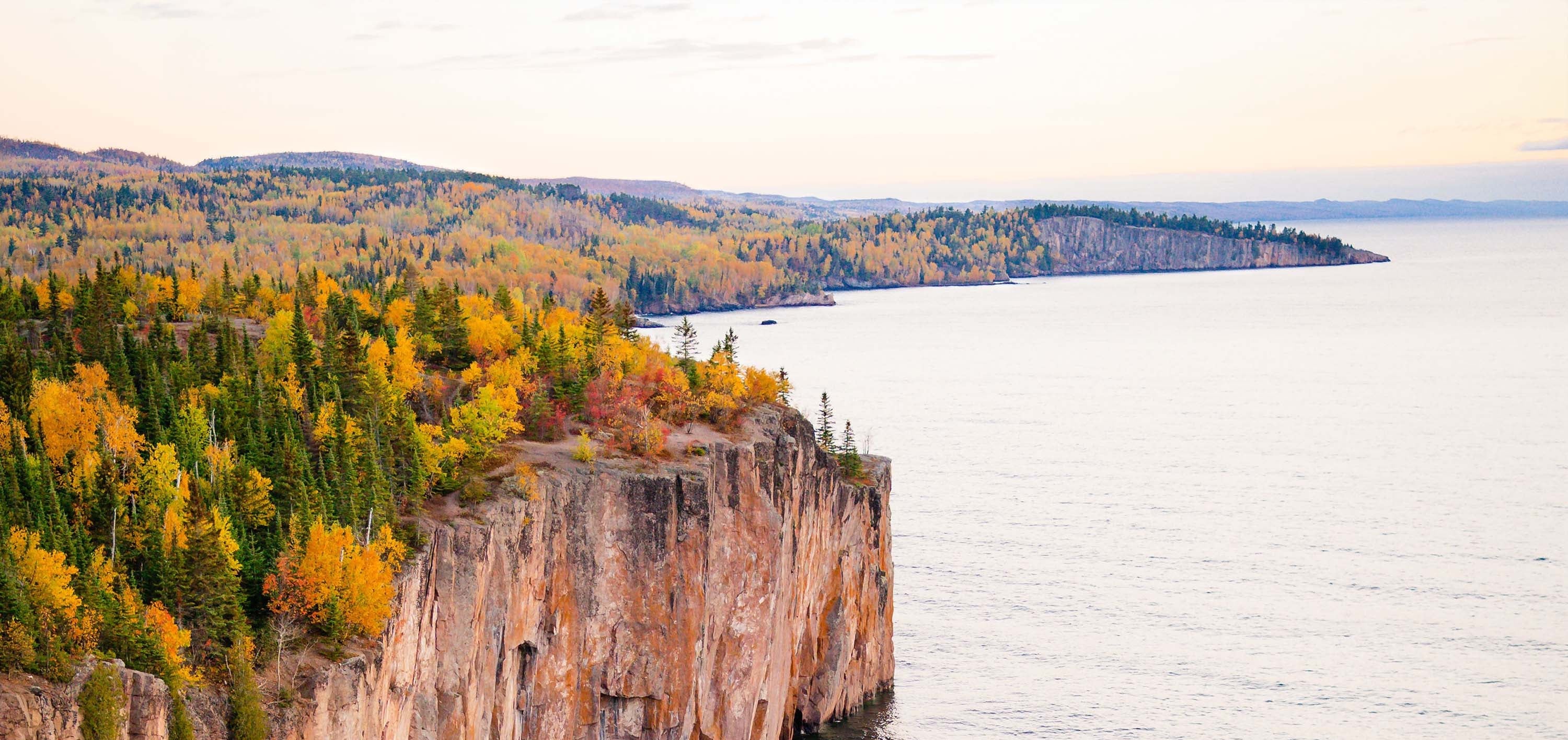 A scenic landscape print showing a rocky cliffside with autumn-colored trees overlooking a large body of water under a pale sky.