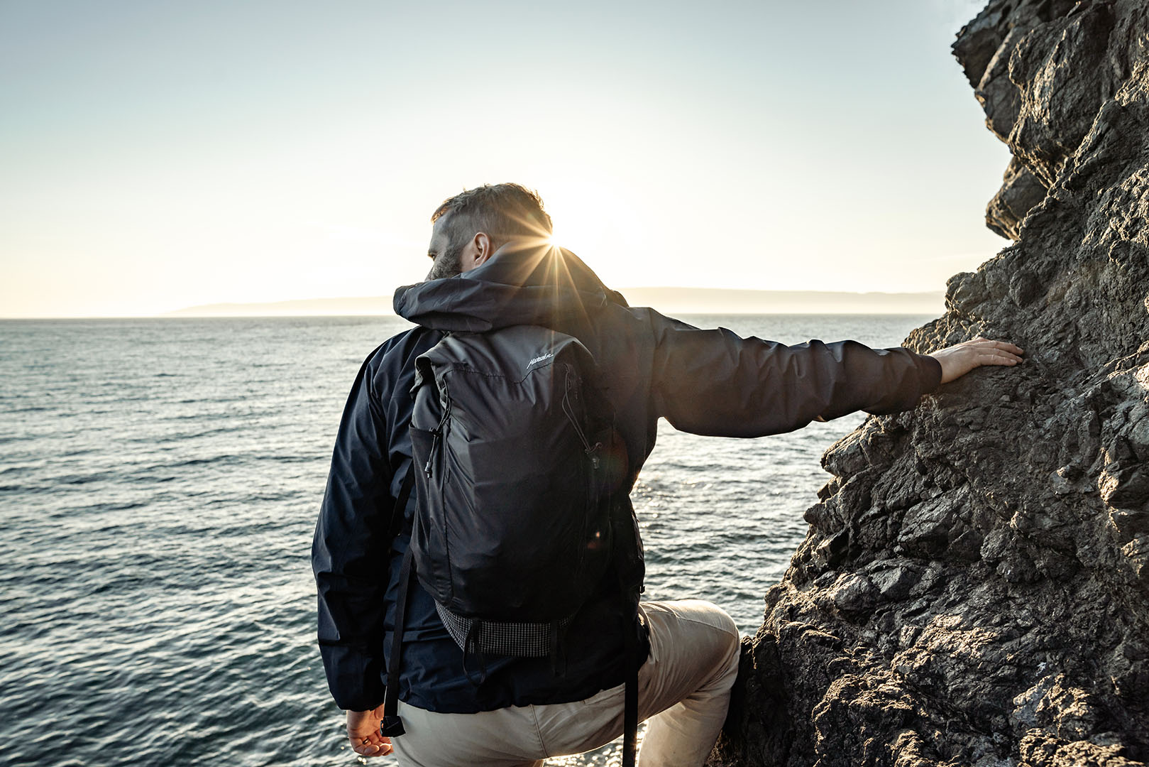 a person on a cliff at a coastal hike traveling with Matador's best waterproof backpack 