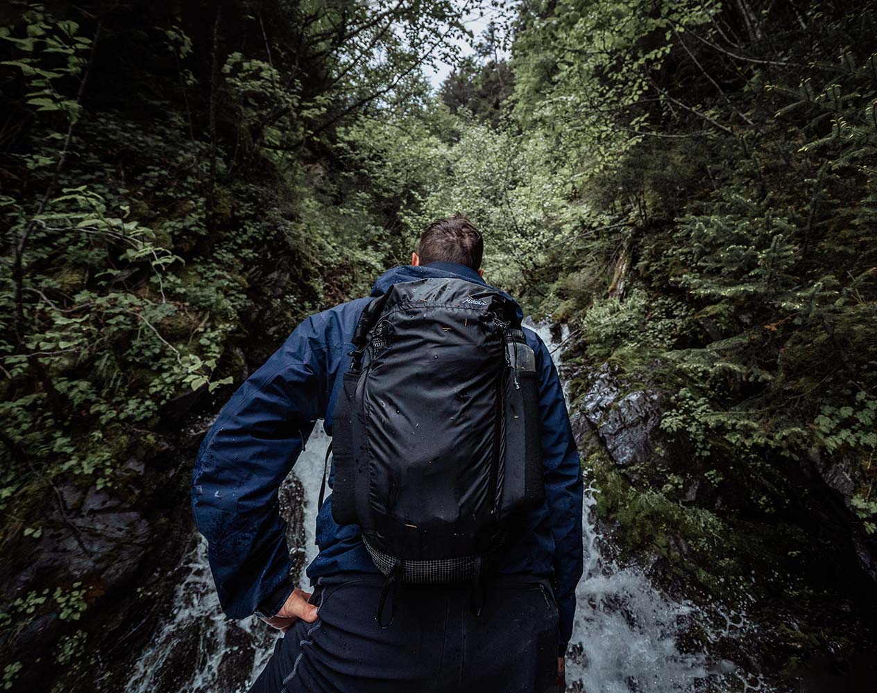 Person with a water-resistant packable backpack walking through a forest with a stream