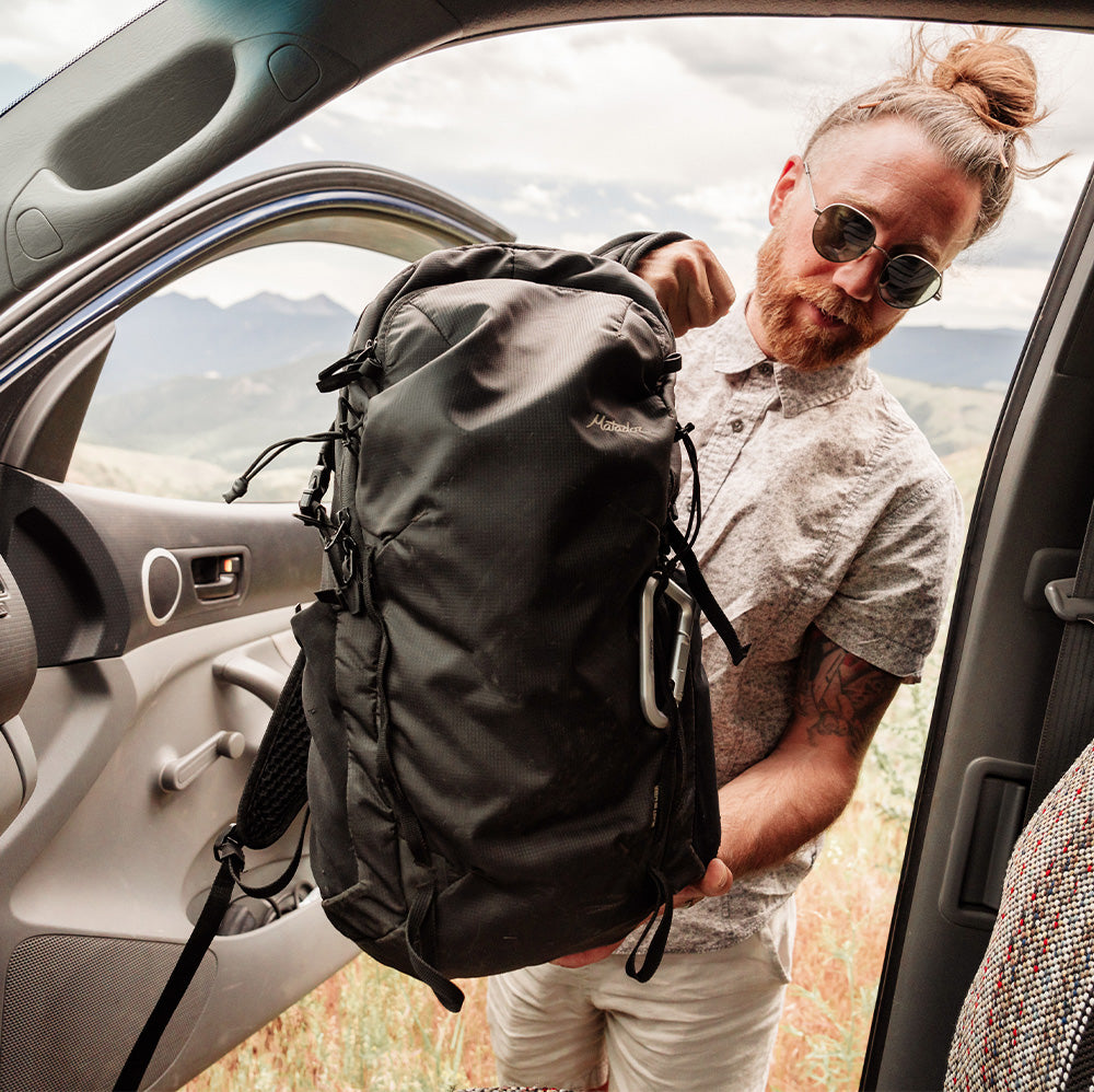 man placing black backpack in his car