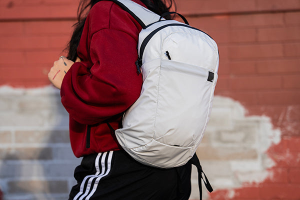 Person wearing a white backpack with a red jacket against a brick wall.