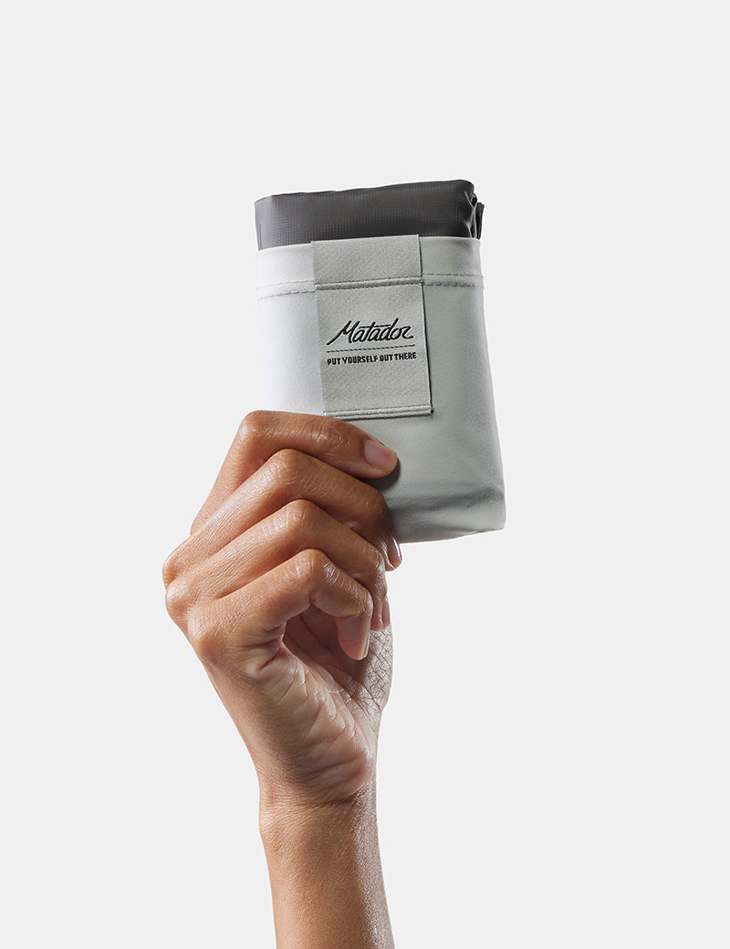 Hand holding a compact pocket blanket on a light gray background