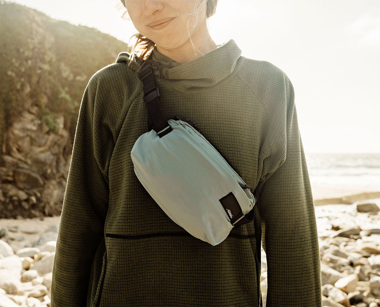 Person wearing a light blue packable sling cross-body outdoors on a beach at sunset