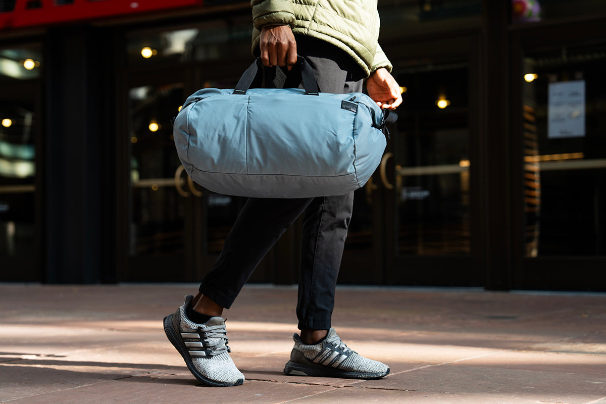 Person holding a blue duffel bag in an urban setting