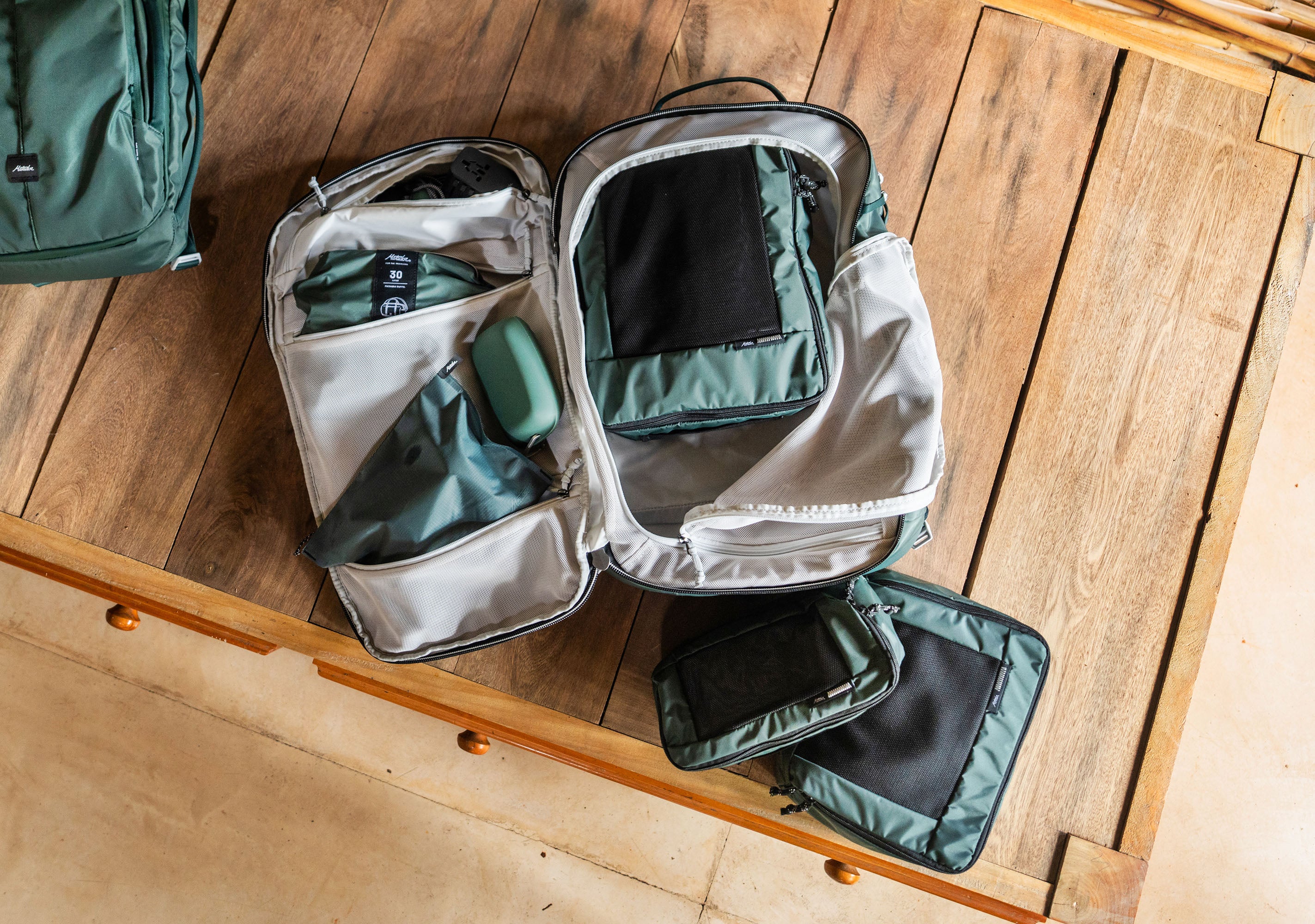 An open green backpack with mesh organizers and packing cube set on a wooden surface, shown with other matching packing toiletries and accessories