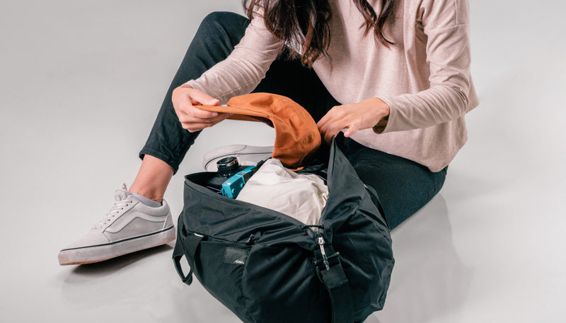 Woman sitting on light gray background adding items to black duffle