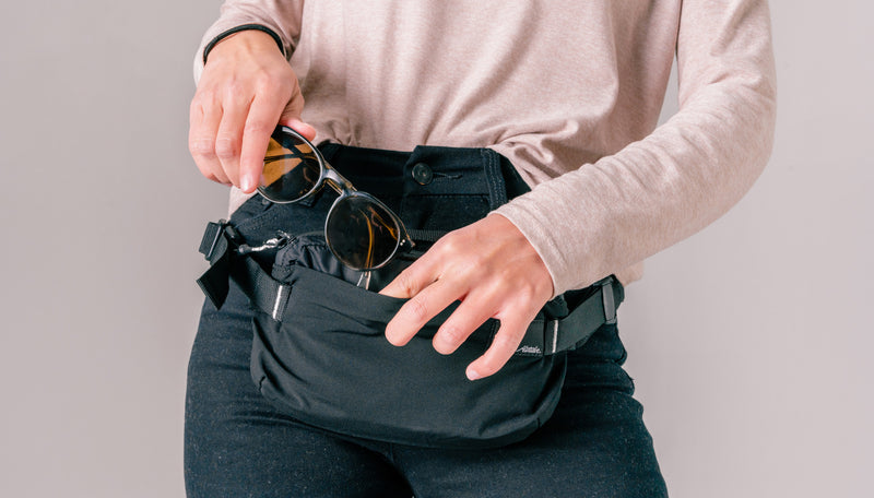 close up view of woman wearing sling at her waist, placing sunglasses inside