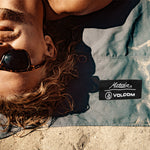 Close up of man laying in sand on charcoal Matador/Volcom beach towel