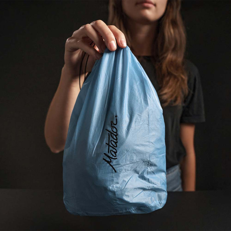Woman on black background holding a full, blue Droplet Stuff Sack