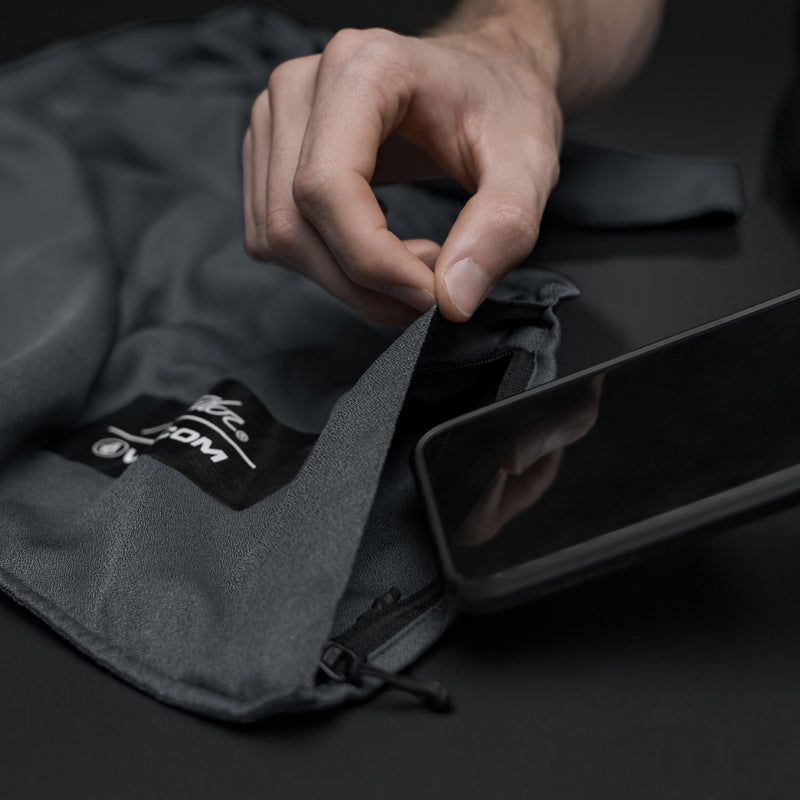 Man placing phone into charcoal beach towel zipper pocket on black background