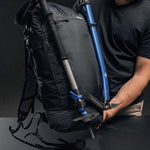 Man holding backpack with trekking pole and ice axe attached