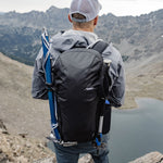 Man standing above alpine lake, wearing Beast28 with ice axe and trekking pole