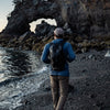 Man walking on rocky beach, wearing backpack