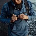 Man on rocky beach, buckling backpack sternum strap
