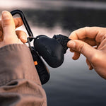 Woman at lake, pulling black Droplet Stuff Sack out of silicone keychain case