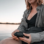 Woman next to lake, holding a Charcoal NanoDry Trek Towel case