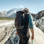 Man wearing backpack, looking out at snowy mountains
