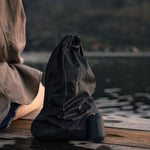 Woman sitting on lake dock with packed up black Droplet Stuff Sack next to its silicone keychain case