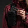 Woman in burgundy pulling passport out of speed stash attached to her backpack strap