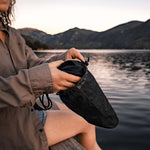 Woman sitting on lake dock, putting black bathing suit into black Droplet