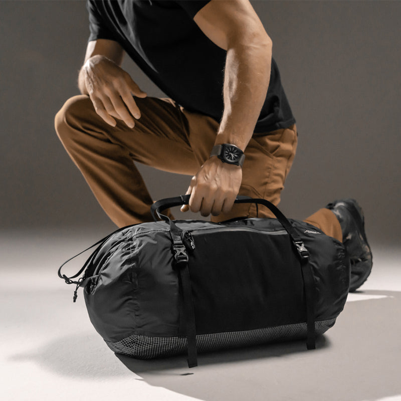 Kneeling man picking up duffle by carry handles