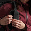 Woman in burgundy jacket securing back of speed stash to her backpack strap