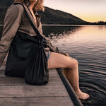 Woman sitting on lake doc with black Droplet attached to her tote bag