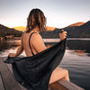 Woman with wet hair sitting on dock, drying herself off with a Charcoal NanoDry towel