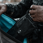 Close up view of motorcyclist placing rain covered dry bag into a waterproof bag