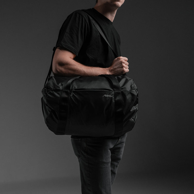 Man with full duffel over his shoulder on black background