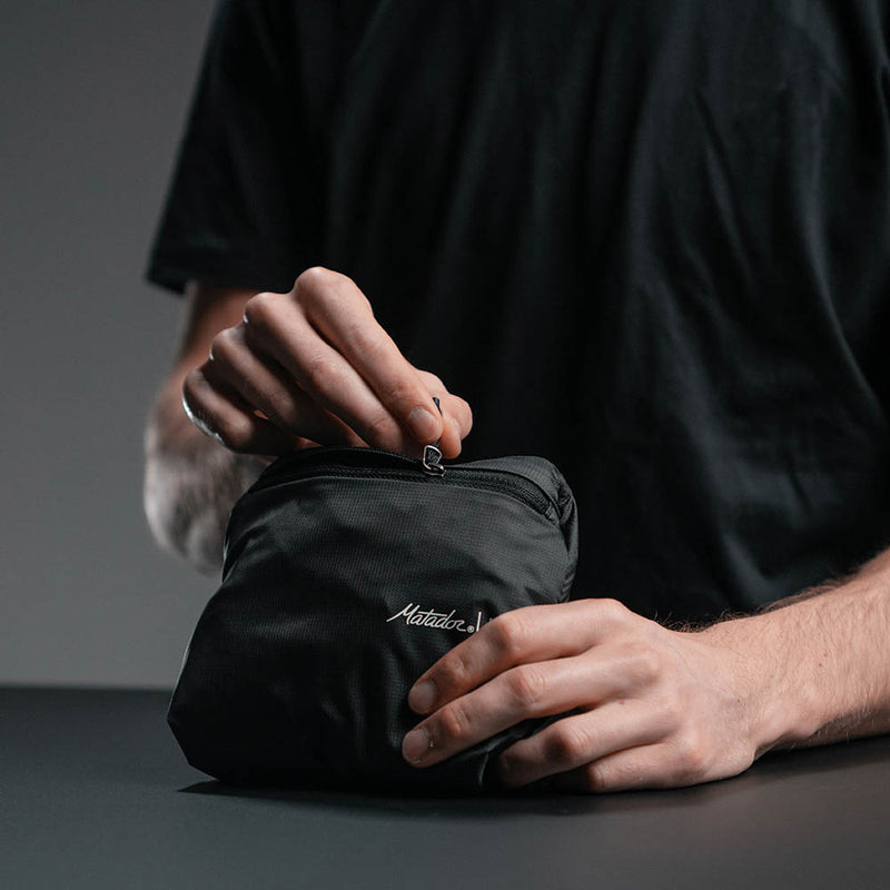 Hands unzipping packed-down backpack pouch