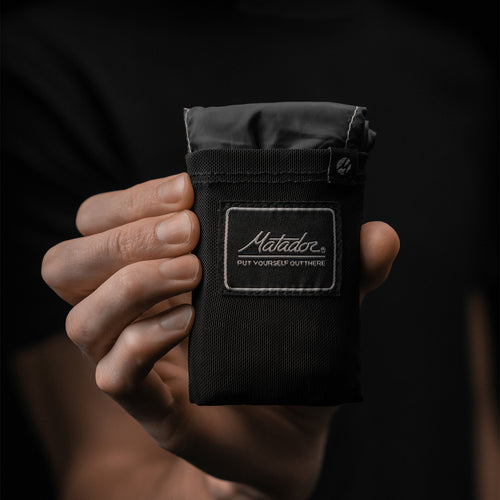 Hand holding packed down pocket blanket on black background