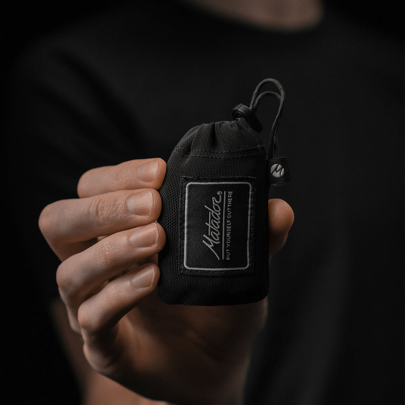 Hand holding small packed down pouch on black background