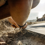 Man on sunset beach, staking pocket blanket into sand