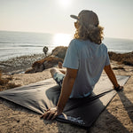 Man at sunset beach, sitting on pocket blanket