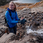 Woman at alpine river drying hands with trek towel